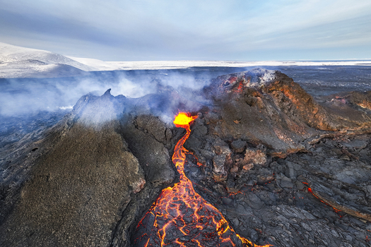 Aerial view of molten lava flows like fiery rivers from the volcanic eruption contrasting against the stark snow covered landscape Grindav&iacute;kurb&aelig;r Iceland.