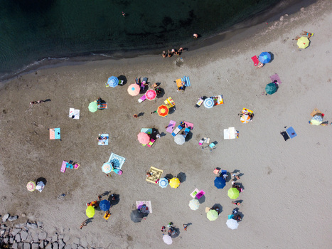 Aerial view of colorful beach umbrellas and towels scattered on the sand with people sunbathing near the dark sea water in San Lorenzo Liguria Italy.
