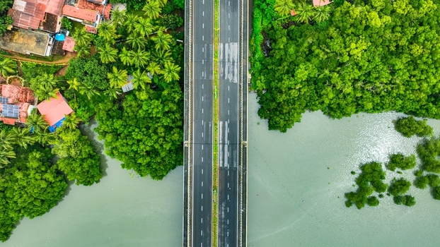 Aerial view of a modern bridge spanning the Galgibaga River surrounded by dense mangrove forests lush palm trees and residential houses in Canacona Goa India.