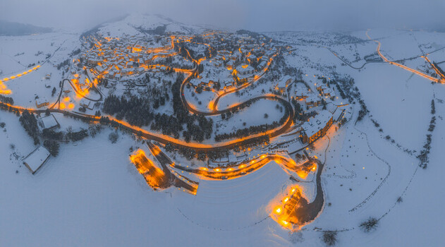 Aerial view of the snow covered town of Rivisondoli at dusk with illuminated streets and buildings winding through the winter landscape in Rivisondoli Abruzzo Italy.