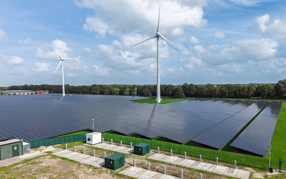 Aerial view of a large solar farm with rows of photovoltaic panels and wind turbines set in a green landscape in Warmenhuizen North Holland Netherlands.