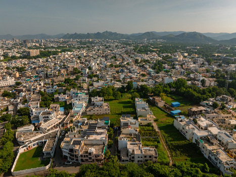 Aerial view of the cityscape of Udaipur with residential buildings lush green patches and distant hills under a clear sky in Udaipur Rajasthan India.