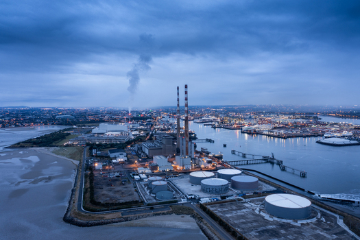 Aerial view of Poolbeg Power Station with its iconic striped chimneys industrial storage tanks and the Dublin city skyline under a twilight sky Dublin 4 County Dublin Ireland. Aerial view of Poolbeg Power Station with its iconic striped chimneys industrial storage tanks and the Dublin city skyline under a twilight sky Dublin 4 County Dublin Ireland.
