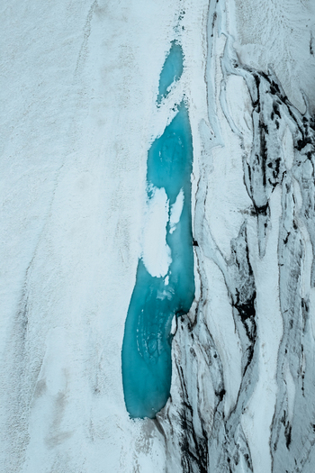 Aerial view of the vibrant blue meltwater pool within the white ice of Vatnajokull glacier in Iceland.