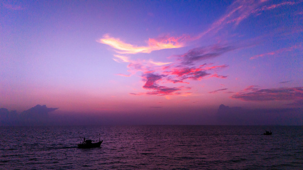 Aerial view of a fishing boat on the calm sea under a vibrant purple and pink sunset sky at Varca Beach SOUTH GOA Goa India.