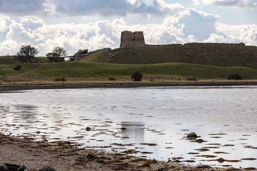 View of the historic Kalo Castle ruins situated on a grassy hill overlooking the calm waters of the bay in Ronde Jutland Denmark. View of the historic Kalo Castle ruins situated on a grassy hill overlooking the calm waters of the bay in Ronde Jutland Denmark.
