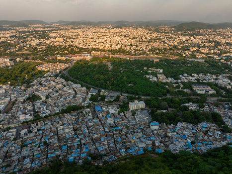 Aerial view of the dense urban landscape featuring traditional rooftops modern buildings and lush green parks set against distant hills in Udaipur Rajasthan India.