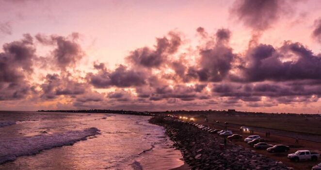 Aerial view of a coastal road with parked cars along a rocky breakwater at sunset with purple clouds over the ocean in Ghana. Aerial view of a coastal road with parked cars along a rocky breakwater at sunset with purple clouds over the ocean in Ghana.