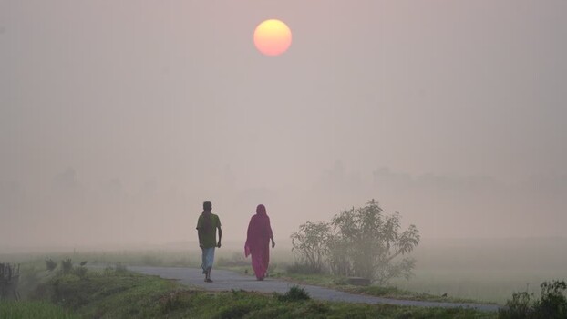 View of a man and woman walking on a path at sunrise Bangladesh.