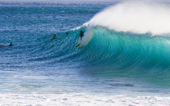 View of a surfer riding a large breaking wave at Banzai Pipeline with other surfers in the turquoise water in Haleiwa Hawaii United States.
