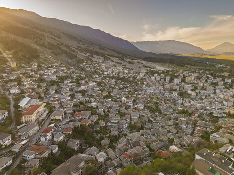 Aerial view of Gjirokaster featuring traditional stone houses with slate roofs narrow streets and surrounding mountains under a warm sunset glow in Gjirokaster Gjirokaster County Albania. Aerial view of Gjirokaster featuring traditional stone houses with slate roofs narrow streets and surrounding mountains under a warm sunset glow in Gjirokaster Gjirokaster County Albania.