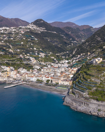 Aerial view of sun kissed buildings cascade down to meet the deep blue sea framed by the rugged verdant mountains Minori Campania Italy. Aerial view of sun kissed buildings cascade down to meet the deep blue sea framed by the rugged verdant mountains Minori Campania Italy.
