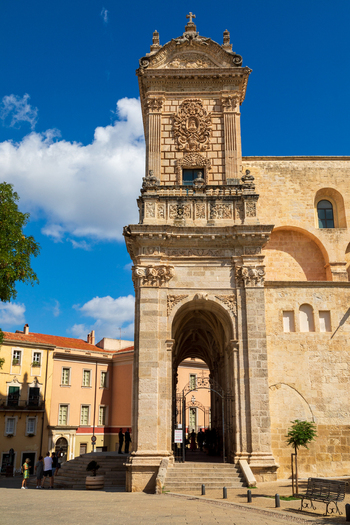 View of the ornate stone facade and bell tower of the Cathedral of Santa Maria in Cagliari featuring intricate carvings and arched doorways in Sardinia Italy.