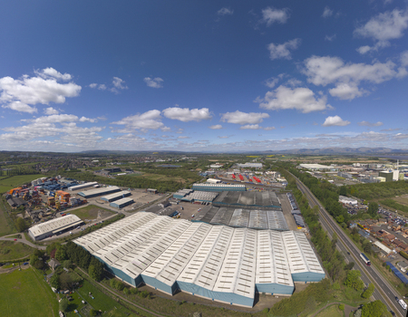 Aerial view of large industrial warehouses and logistics facilities surrounded by green fields under a blue sky with clouds in Grangemouth Scotland United Kingdom.