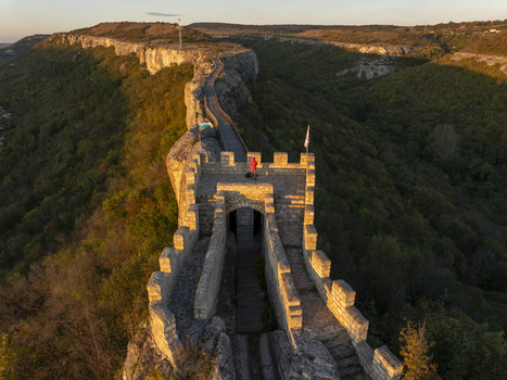 Aerial view of Ovech Fortress with a person standing on the stone ramparts during golden hour overlooking the surrounding forested cliffs and valley in Provadia Varna Bulgaria. Aerial view of Ovech Fortress with a person standing on the stone ramparts during golden hour overlooking the surrounding forested cliffs and valley in Provadia Varna Bulgaria.