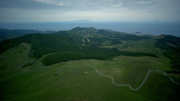 Aerial view of the rolling green hills of Hosono Plateau with winding roads and dense forest overlooking the Pacific Ocean in Higashiizu Shizuoka Japan. Aerial view of the rolling green hills of Hosono Plateau with winding roads and dense forest overlooking the Pacific Ocean in Higashiizu Shizuoka Japan.