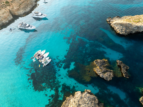 Aerial view of boats resting on the turquoise waters near the rocky shores of Blue Lagoon Comino Malta. Aerial view of boats resting on the turquoise waters near the rocky shores of Blue Lagoon Comino Malta.