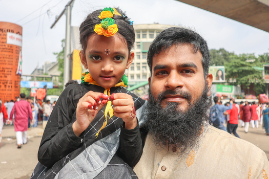 Dhaka Bangladesh 13 April 2026 View of a bearded man cradles a young girl vibrant in yellow and green floral adornments and crimson tipped fingers amidst a bustling street.