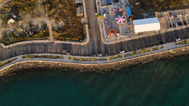 Aerial view of a coastal road with a small carnival colorful tents parked cars and a rocky shoreline bordering the clear sea in Sorong Southwest Papua Indonesia. Aerial view of a coastal road with a small carnival colorful tents parked cars and a rocky shoreline bordering the clear sea in Sorong Southwest Papua Indonesia.