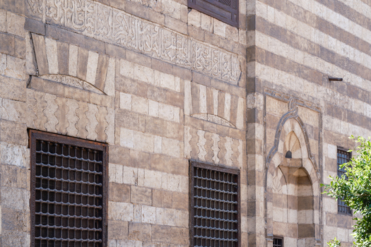 View of the intricate Mamluk architecture of Al Ghuri Dome featuring ablaq masonry Arabic calligraphy and ornate window grilles Cairo Egypt. View of the intricate Mamluk architecture of Al Ghuri Dome featuring ablaq masonry Arabic calligraphy and ornate window grilles Cairo Egypt.