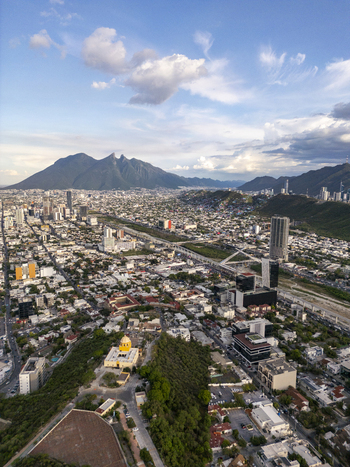 Aerial view of the city of Monterrey with the iconic Cerro de la Silla mountain in the background featuring urban architecture roads and green spaces in Monterrey Nuevo Leon Mexico.