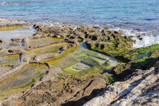 View of the rugged coastline where the turquoise sea meets the rocky shore creating shallow pools reflecting the clear sky Marsaskala Malta. View of the rugged coastline where the turquoise sea meets the rocky shore creating shallow pools reflecting the clear sky Marsaskala Malta.