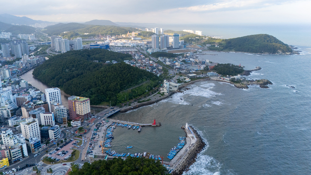Aerial view of Songjeong dong featuring a small fishing harbor with blue boats a red lighthouse coastal cliffs and urban buildings along the shoreline in Busan Busan South Korea. Aerial view of Songjeong dong featuring a small fishing harbor with blue boats a red lighthouse coastal cliffs and urban buildings along the shoreline in Busan Busan South Korea.