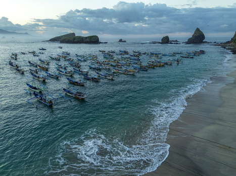 Aerial view of Papuma Beach with numerous traditional fishing boats anchored in the turquoise bay near the sandy coastline in Jember East Java Indonesia. Aerial view of Papuma Beach with numerous traditional fishing boats anchored in the turquoise bay near the sandy coastline in Jember East Java Indonesia.