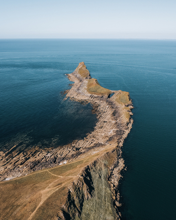 Aerial view of Worms Head Causeway with its rocky coastline extending into the blue sea in Rhossili Wales United Kingdom.