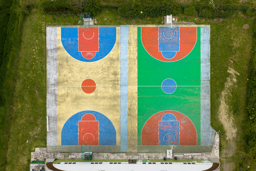 Aerial view of a colorful outdoor basketball court with vibrant blue red green and yellow painted sections surrounded by green grass in San Giovanni Valdarno Tuscany Italy.