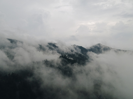 Aerial view of lush green mountain peaks shrouded in thick white clouds and mist under an overcast sky Tawangmangu Central Java Indonesia.
