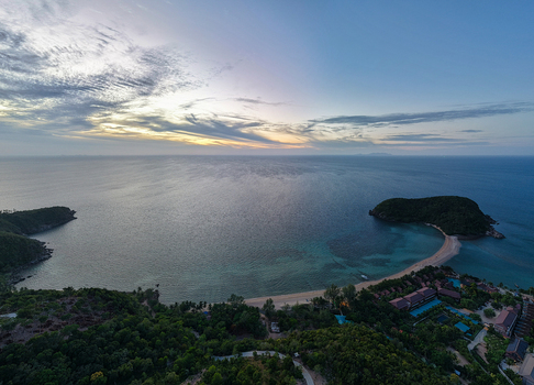 Aerial view of the Ko Pha Ngan coastline with lush vegetation sandy beach turquoise waters and a small island connected by a sandbar at sunset in Ko Pha ngan District Surat Thani Thailand.