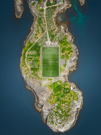 Aerial view of the famous football pitch surrounded by rocky terrain lush green patches and the deep blue waters of the Norwegian Sea in Henningsvaer Nordland Norway.