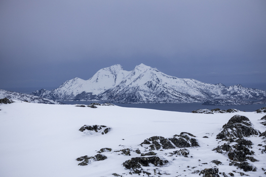 View of snow covered mountain peaks and a calm fjord under an overcast sky Kvaloya Troms Norway.