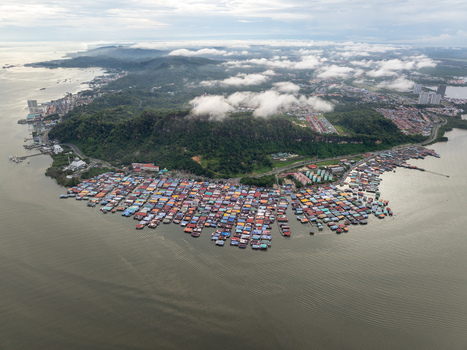 Aerial view of the colorful stilt houses of a water village along the coastline with lush green hills and misty clouds in Kota Kinabalu Sabah Malaysia. Aerial view of the colorful stilt houses of a water village along the coastline with lush green hills and misty clouds in Kota Kinabalu Sabah Malaysia.