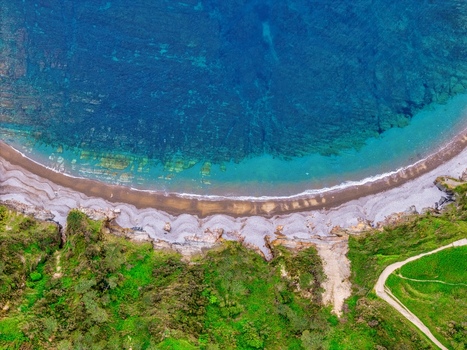 Aerial view of Silence Beach Viewpoint with its turquoise waters crescent shaped shoreline and lush green cliffs in Cudillero Asturias Spain.