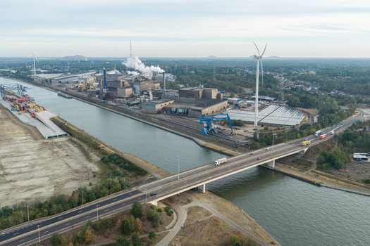 Genk Belgium 27 August 2026 Aerial view of Genk Cargo Connect industrial site featuring a canal bridge with traffic wind turbines and solar panels in an industrial landscape.