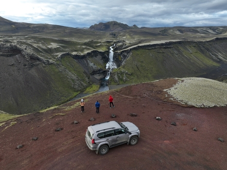 Aerial view of Eldgja canyon featuring a waterfall a parked 4x4 vehicle and three people standing on a red volcanic ridge in Kirkjubaejarklaustur Skaftarthreppur Iceland. Aerial view of Eldgja canyon featuring a waterfall a parked 4x4 vehicle and three people standing on a red volcanic ridge in Kirkjubaejarklaustur Skaftarthreppur Iceland.