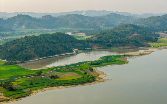 Aerial view of Lak Lake surrounded by lush green rice paddies and rolling hills under a soft sky in Lien Son Lak Dak Lak Vietnam. Aerial view of Lak Lake surrounded by lush green rice paddies and rolling hills under a soft sky in Lien Son Lak Dak Lak Vietnam.