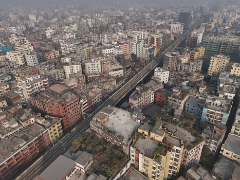 Aerial view of the dense urban landscape of Dhaka featuring the elevated metro rail line winding through residential apartment buildings and city infrastructure in Dhaka Bangladesh. Aerial view of the dense urban landscape of Dhaka featuring the elevated metro rail line winding through residential apartment buildings and city infrastructure in Dhaka Bangladesh.