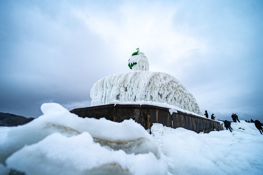 View of the frozen Molenfeuer Sassnitz lighthouse covered in thick ice with people walking on the snowy pier under a cloudy winter sky in Sassnitz Mecklenburg Vorpommern Germany.