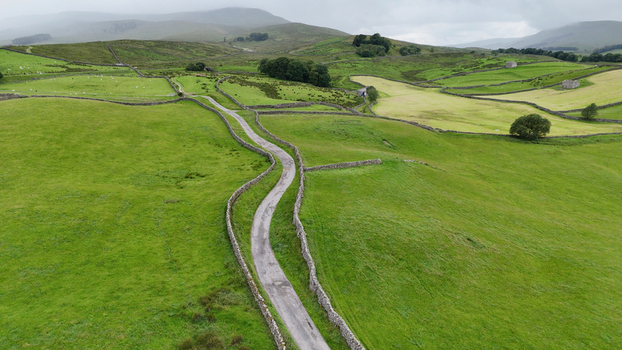 Yorkshire UK Aerial view of a narrow winding road cutting through vibrant green fields divided by traditional dry stone walls in a misty rural landscape. Yorkshire UK Aerial view of a narrow winding road cutting through vibrant green fields divided by traditional dry stone walls in a misty rural landscape.