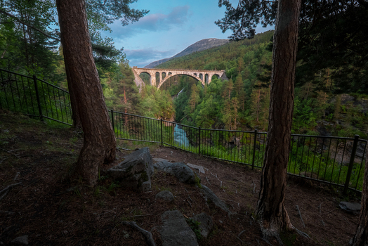 View of Kylling Bridge spanning the Rauma River framed by pine trees and lush forest in the valley of Rauma Municipality More og Romsdal Norway. View of Kylling Bridge spanning the Rauma River framed by pine trees and lush forest in the valley of Rauma Municipality More og Romsdal Norway.