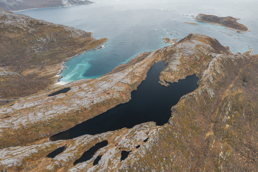 Aerial view of the rugged rocky landscape and dark mountain lake on Senja island with coastal waters in the background in Senja Troms Norway.