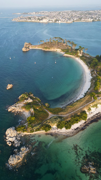 Aerial view of the coastline where the white sands embrace the turquoise sea a rugged headland adorned with lush greenery Roscoff Finistere France.