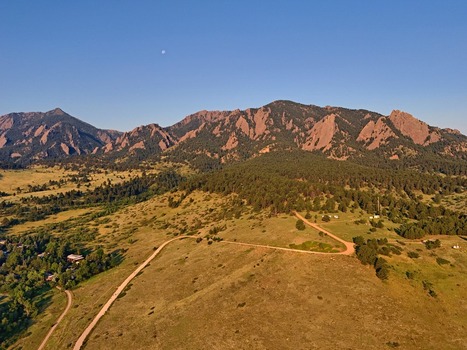 Aerial view of the NCAR and UCAR Foothills Laboratory nestled against the iconic Flatirons mountain range with winding dirt trails and pine forests in Boulder Colorado United States.