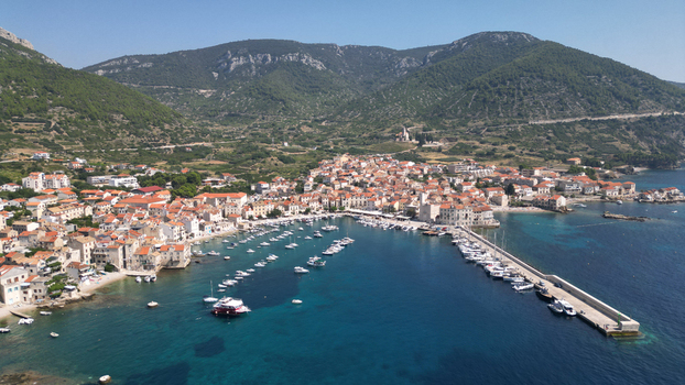 Aerial view of the coastal town of Komiza featuring its harbor with boats stone houses with red roofs and a long pier against green hills in Komiza Split Dalmatia County Croatia.