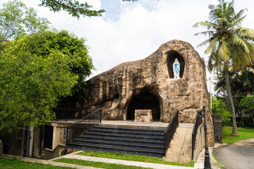 View of a religious grotto with a statue of the Virgin Mary in a rock niche surrounded by lush tropical greenery and palm trees in Galle Southern Province Sri Lanka.