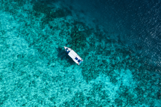 Aerial view of a small white boat floating in the clear turquoise waters of a coral reef in Vashafaru Haa Alif Atoll Maldives. Aerial view of a small white boat floating in the clear turquoise waters of a coral reef in Vashafaru Haa Alif Atoll Maldives.