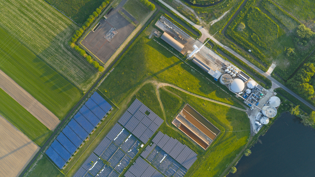 Aerial view of Wabico BV facility featuring solar panel arrays a wind turbine and industrial tanks surrounded by green agricultural fields in Waalwijk Noord Brabant Netherlands.